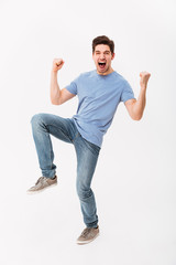 Full-length photo of happy man 30s in casual t-shirt and jeans rejoicing with clenching fists, isolated over white background