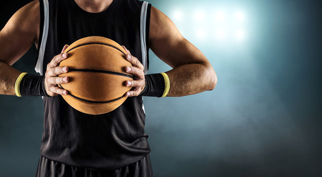 Basketball ball in a male hands, player in black with orange spo