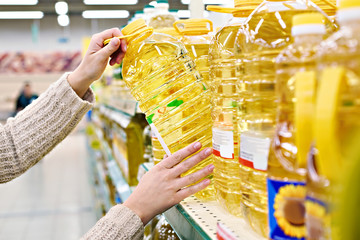 Buyer takes sunflower oil from shelf in store