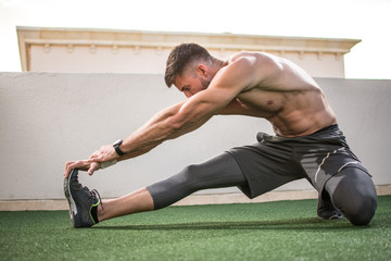 Muscular sportsman warming up before sports training outdoors.