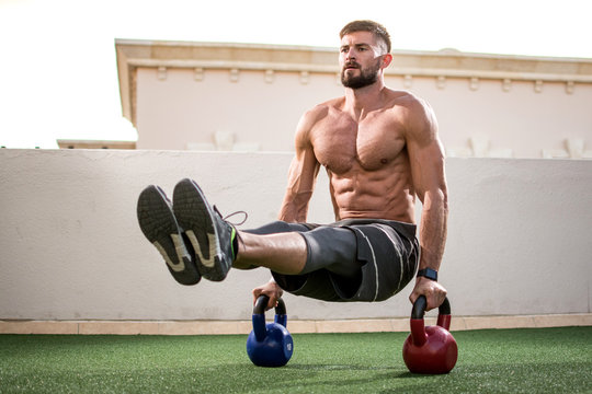 Muscular shirtless man workout with kettlebells in L Sit position outdoors.  Stock Photo