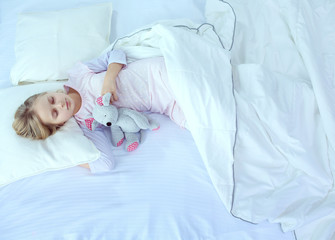 Obraz na płótnie Canvas Child little girl sleeps in the bed with a toy teddy bear