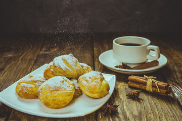 Delicious eclairs sprinkled with icing sugar, stand on a wooden table. Copy spase.