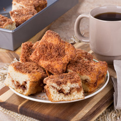 Pile of cinnamon swirl coffee cake on a plate and cup of coffee in background