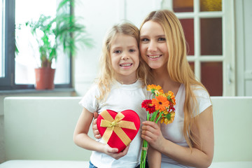 Fototapeta na wymiar Beautiful cheerful mother and a little smiling daughter embrace with gifts in their hands and look at the camera. Birthday. March 8. Women's Day.