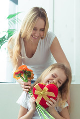 Fototapeta na wymiar Surprise for the daughter. Beautiful cheerful mother gives her little smiling daughter a gift and a bouquet of flowers. Birthday. March 8. Women's Day.
