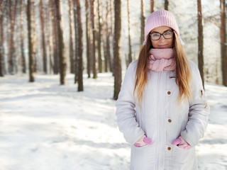 Adorable happy young blonde woman in pink knitted hat scarf having fun strolling snowy winter forest in nature