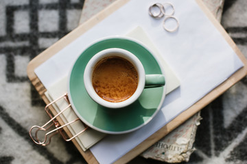Delicious freshly brewed morning espresso coffee with a beautiful crema in a green ceramic cup with a saucer standing on a notepad and an old book, wool background, top view