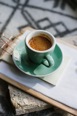 Delicious freshly brewed morning espresso coffee with a beautiful crema in a green ceramic cup with a saucer standing on a notepad and an old book, wool background, top view