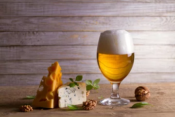 Poster Beer and cheese. Glass of beer with cheese, walnuts and basil on wooden background. Ale and food concept © freeskyline