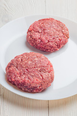 Raw hamburger patties on white plate