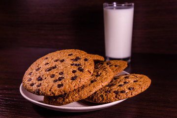 Plate with chocolate chip cookies and a glass of milk on a dark wooden table