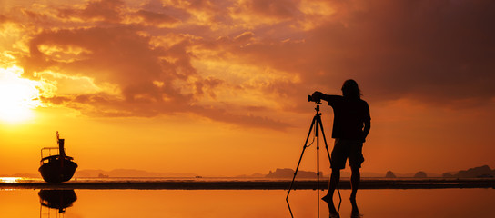 Silhouette of a photographer with tripod on beautiful tropical sunset