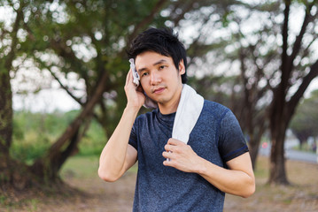 young sporty man resting and wiping his sweat with a towel after workout sport exercises outdoors at park