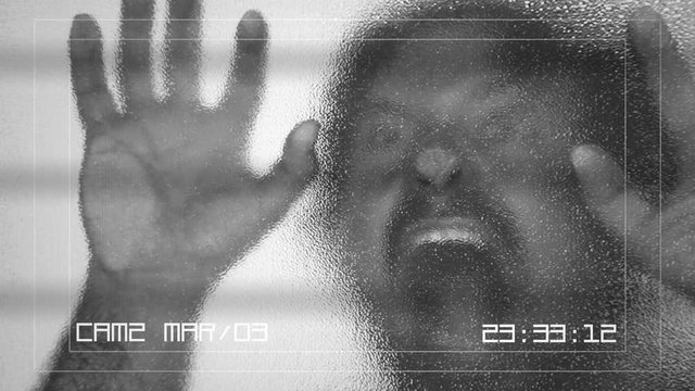 A CCTV security camera screen: a zombie lurking behind a frosted glass door and attacking the viewer. Horror Halloween themed shot.
