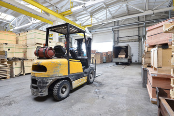 The forklift is old and scratched in a large and light warehouse. Yellow color