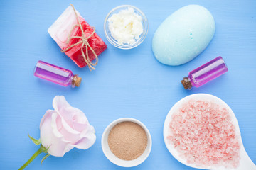 Spa and natural cosmetics concept. Set of sea salt, rose, natural clay ,shea oil, glass bottles and other spa treatment tools on the blue wooden background. Top view. Space for a text. Close up.