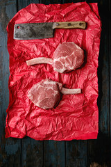 Raw uncooked black angus beef tomahawk steaks on bones served with vintage butcher cleaver on red...