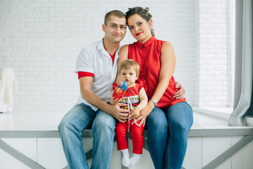 Young family of three sitting in white room. Little girl playing with russian doll. Mother father...