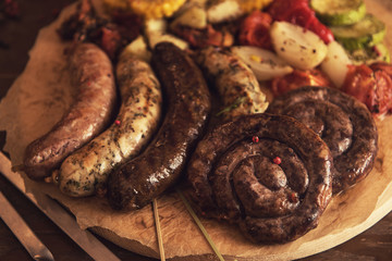Grilled different meat and fish sausages with vegetables and spices on wooden background