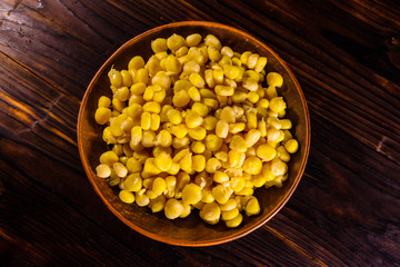 Ceramic plate with canned corn seeds on wooden table. Top view