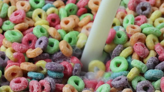 Very close video of adding milk to generic dry sugar coated fruity flavored breakfast cereal.