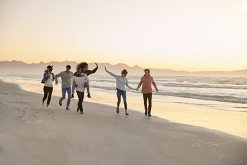 Group Of Friends Having Fun Running Along Winter Beach Together