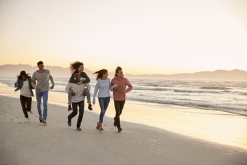 Group Of Friends Having Fun Running Along Winter Beach Together