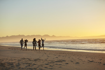 Silhouette Of Friends Having Fun Running Along Winter Beach