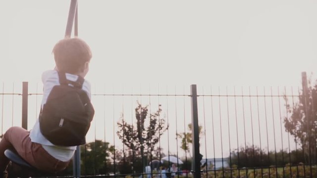 Mother pushes son on a playground zipline. Slow motion. Happy boy rides a long rope swing zip wire. Family together.