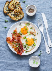 Traditional breakfast or snack - fried eggs, bacon, grilled bread on blue background, top view. Flat lay