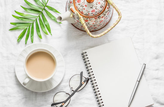 Masala tea, teapot, notepad, glasses, pen, green flower leaf on white background, top view. Morning inspiration planning. Flat lay