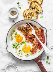 Traditional breakfast or snack - fried eggs, bacon, grilled bread on light background, top view. Flat lay