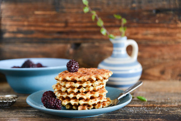 Dessert: round waffles with fresh berries blackberries and icing sugar on a wooden background.
