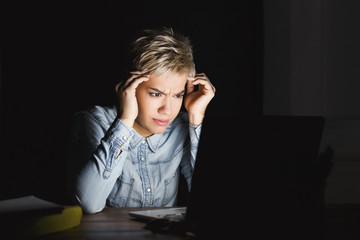 Tired woman with laptop at dark home office copy space