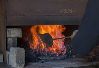 The blacksmith uses an old shovel to stoke up the flames inside the coal forge for the purpose of working metal.