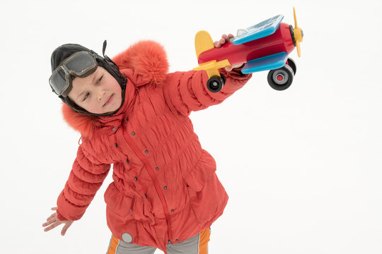 A funny girl in flying glasses and pilot's helmet and red ski jacket. Kid plays with toy plane, introducing himself as pilot. Girl is happy to spend his holidays in village. Winter Joys and Snow