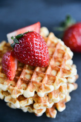 Dessert: round waffles with fresh strawberry berries on dark background.