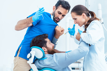 Low-angle view of a funny dentist or dental surgeon acting crazy in front of his female assistant,...