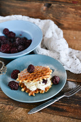 Dessert: round waffles with whipped cream and fresh berries blackberries and icing sugar on a wooden background.