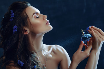 Close up studio portrait of young beautiful woman holding, spraying, using perfume in blue bottle....
