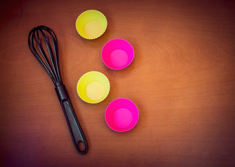 Colorful cupcake silicon baking cups and black whisk over wooden background