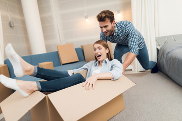 Young couple having fun while moving to new apartment. Moving newlyweds. Girl is sitting in a box.