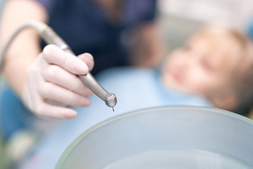 Close-up of doctors hand with dental drill machine. Blurred kid in chair  at stomatology clinic on background. Children visiting stomatology  fear or phobia concept. Tooth healthcare concept