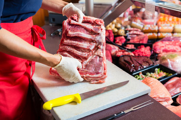 Butcher woman cutting piece of rib meat in her shop with a knife