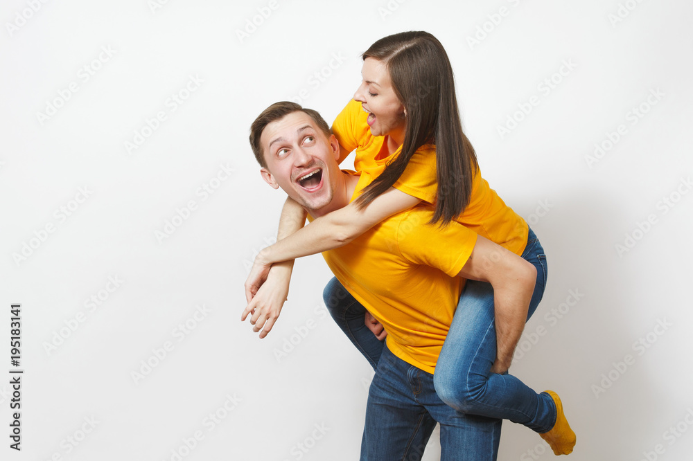 Wall mural Fun inspired young couple, woman sit on man piggyback, fans in yellow cheering favorite team, expressive gesticulating hands isolated on white background. Sport, family leisure, lifestyle concept.