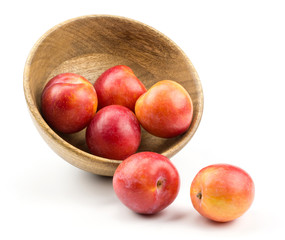 Plums red orange out a wooden bowl isolated on white background.