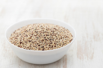 uncooked quinoa in white bowl on wooden background
