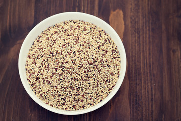 uncooked quinoa in white bowl on wooden background