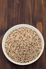 uncooked quinoa in white bowl on wooden background